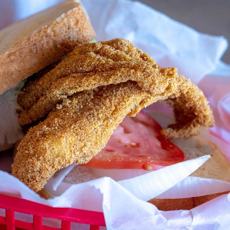 Fried catfish sandwich with tomato and onion in a red basket